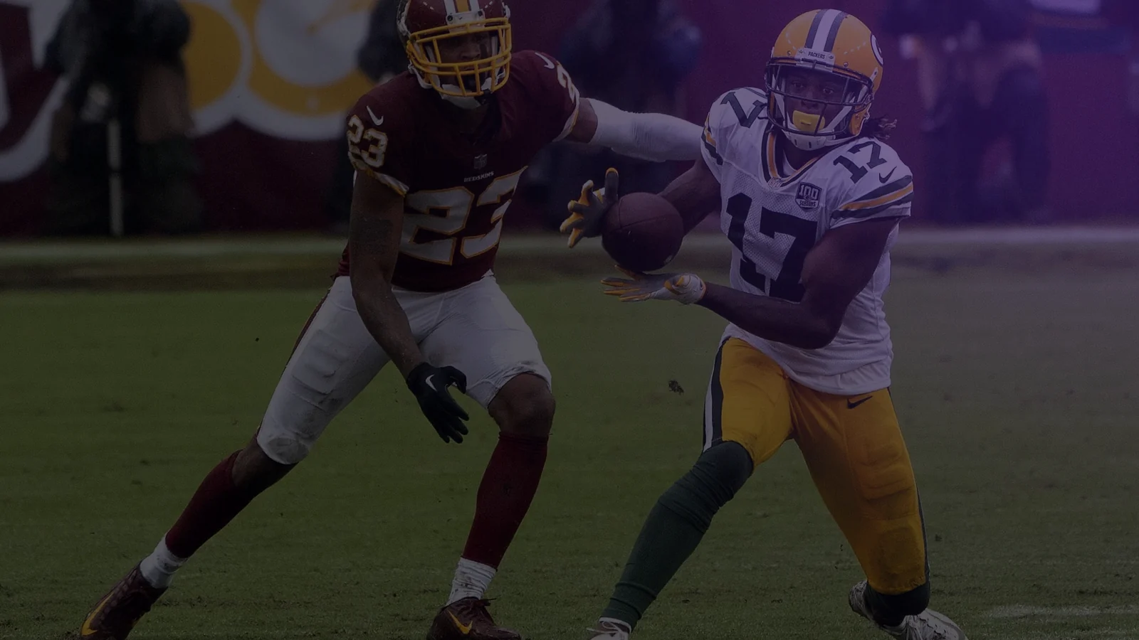 Photo: a receiver reaches for a pass with a cornerback in tight coverage.
